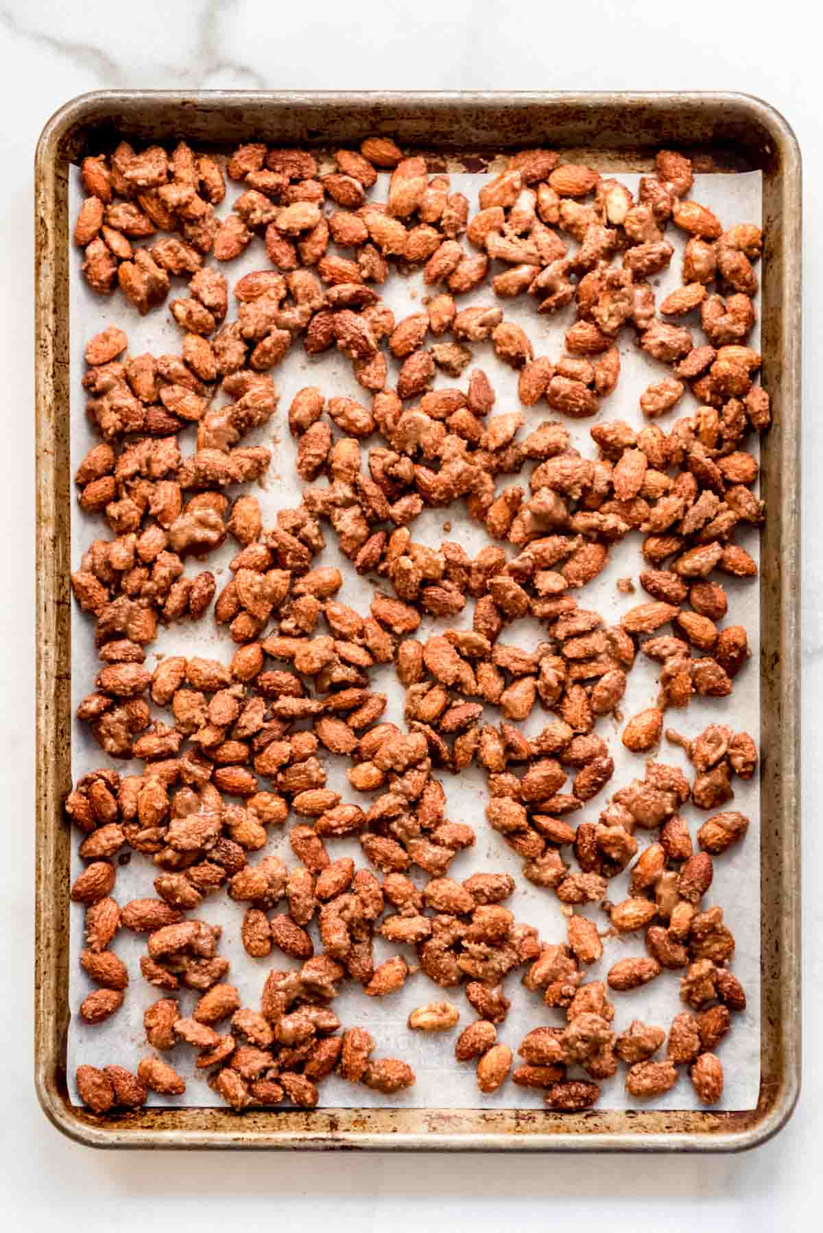 Prepared almonds are spread out on a baking sheet lined with white parchment paper. 