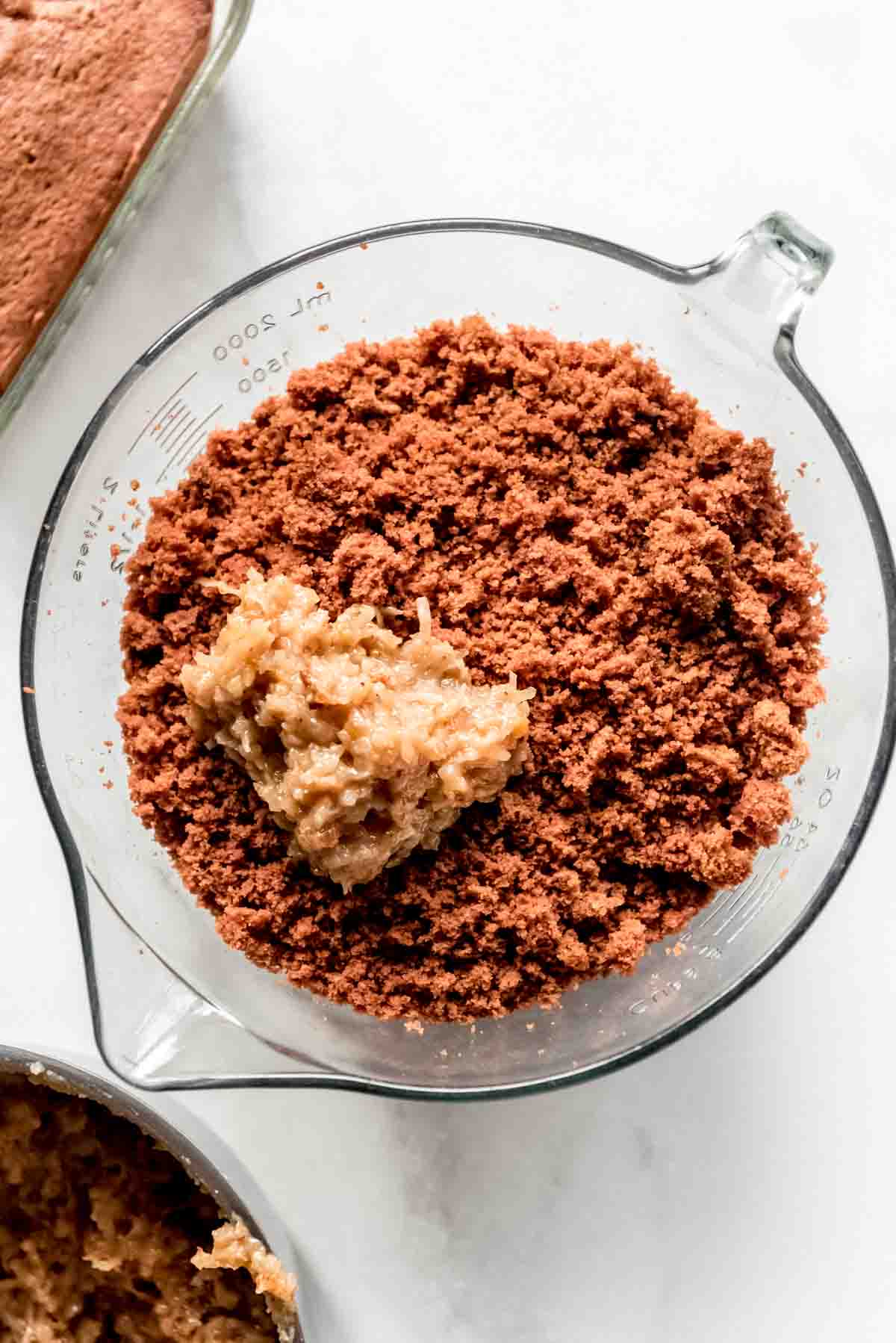 A bowl of german chocolate cake crumbs with a scoop of frosting on top, in a glass bowl. 