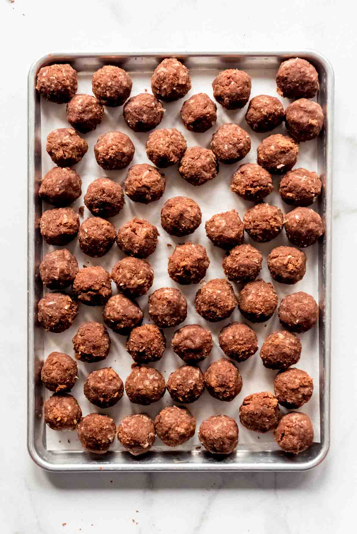 A baking sheet containing many cake balls, resting on a sheet of parchment paper. 