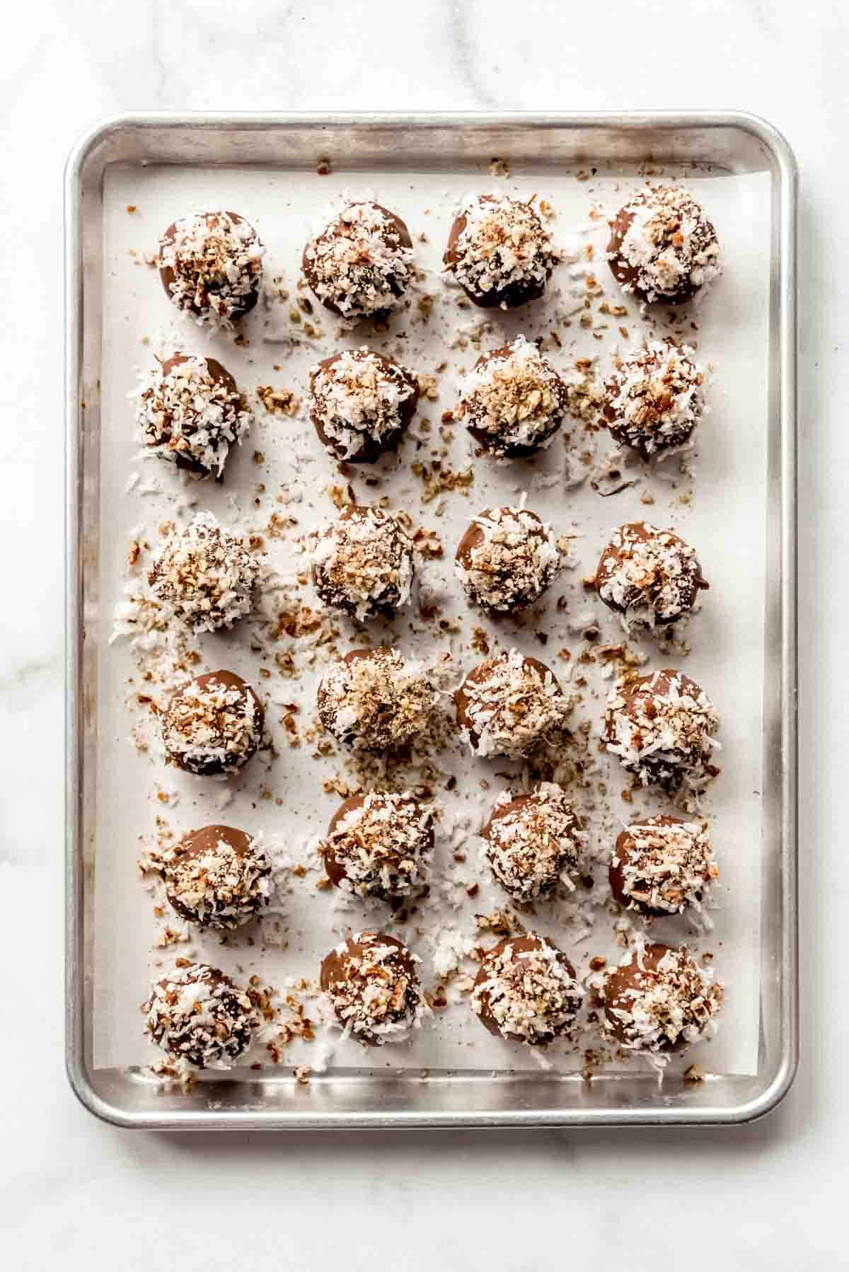 Cake balls on a baking sheet that have been coated with melted chocolate, shredded coconut and chopped pecans. 