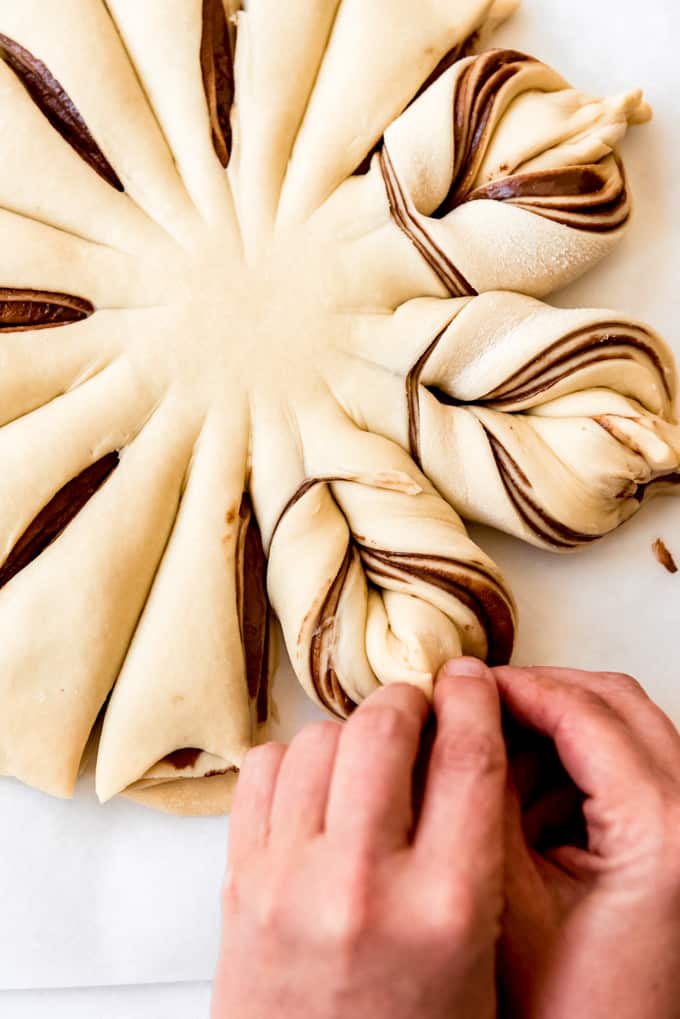 Hands twisting layers of bread dough and nutella into a star shape.