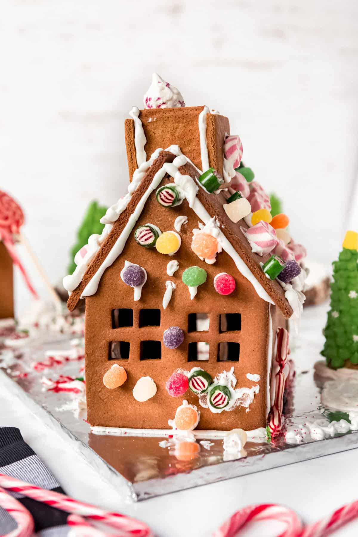 The back of a decorated gingerbread house with multiple cut out windows is shown, along with candy canes in the foreground. 