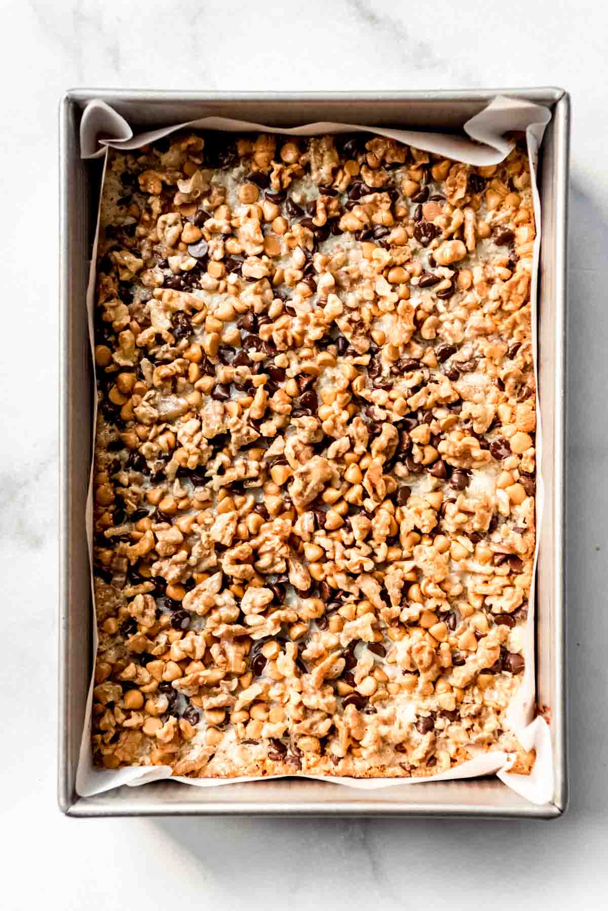 Sweetened condensed milk has been drizzled on top of the layers of ingredients for seven layer bars. 