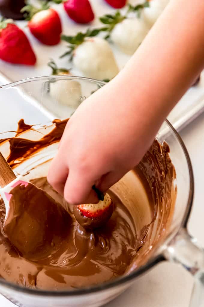 A hand dipping a strawberry in melted chocolate.