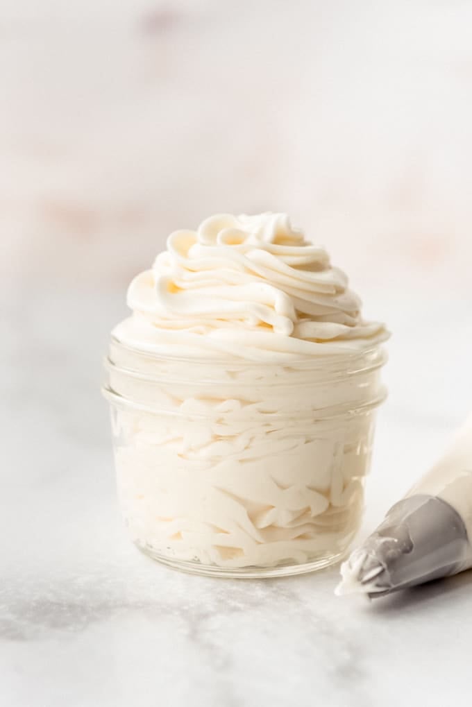 Cream Cheese Frosting piped into a small glass jar, with piping bag nozzle to the side