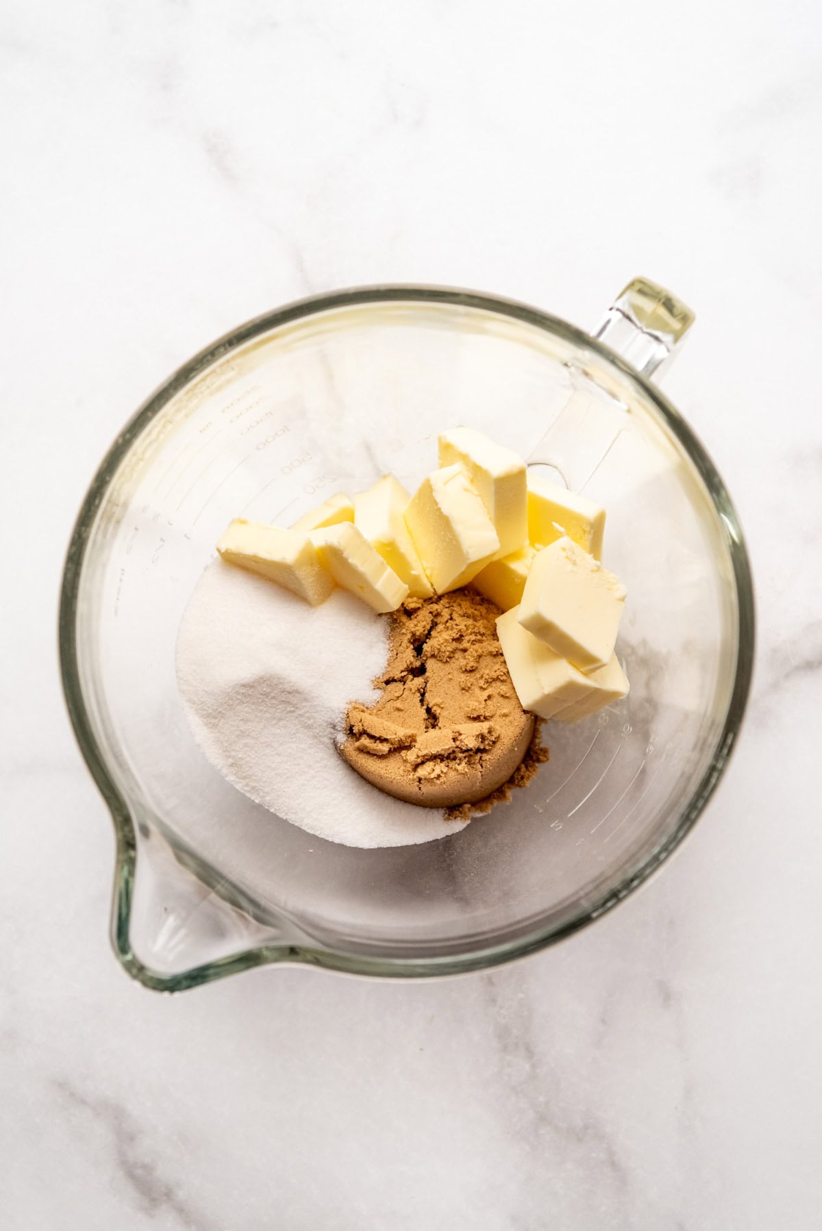 Cold butter, brown sugar, and granulated sugar in a glass mixing bowl.