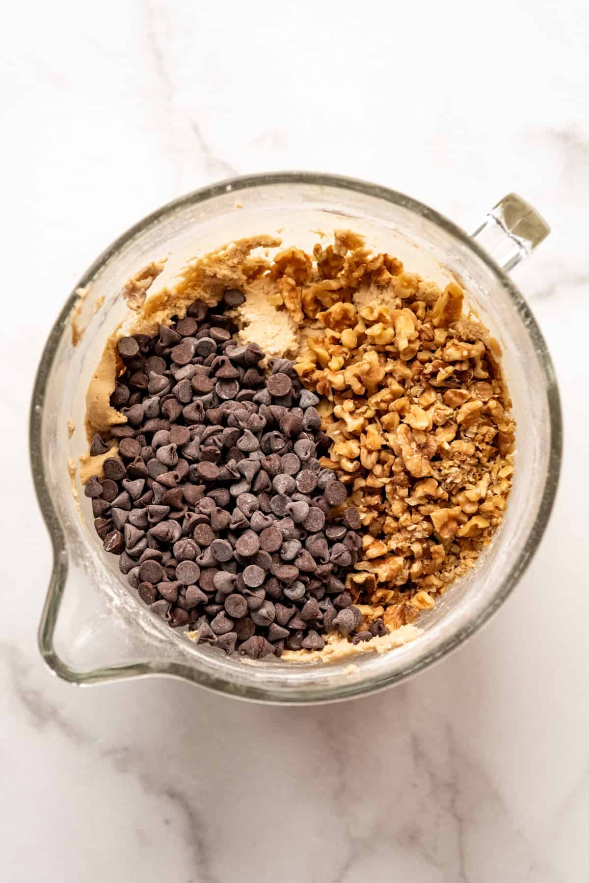 Adding walnuts and chocolate chips to cookie dough in a mixing bowl.