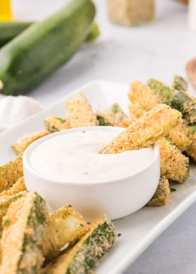 A bowl of ranch dip with a zucchini fry in it.