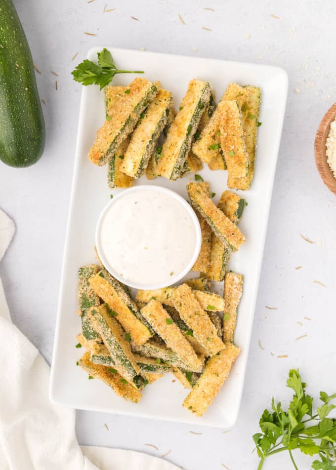 A large plate of parmesan zucchini fries next to a bowl of ranch dip.