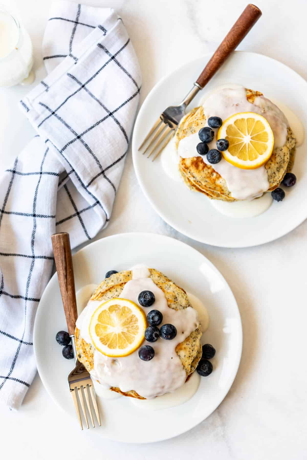 Lemon Poppy Seed Pancakes on white plates with blueberries.