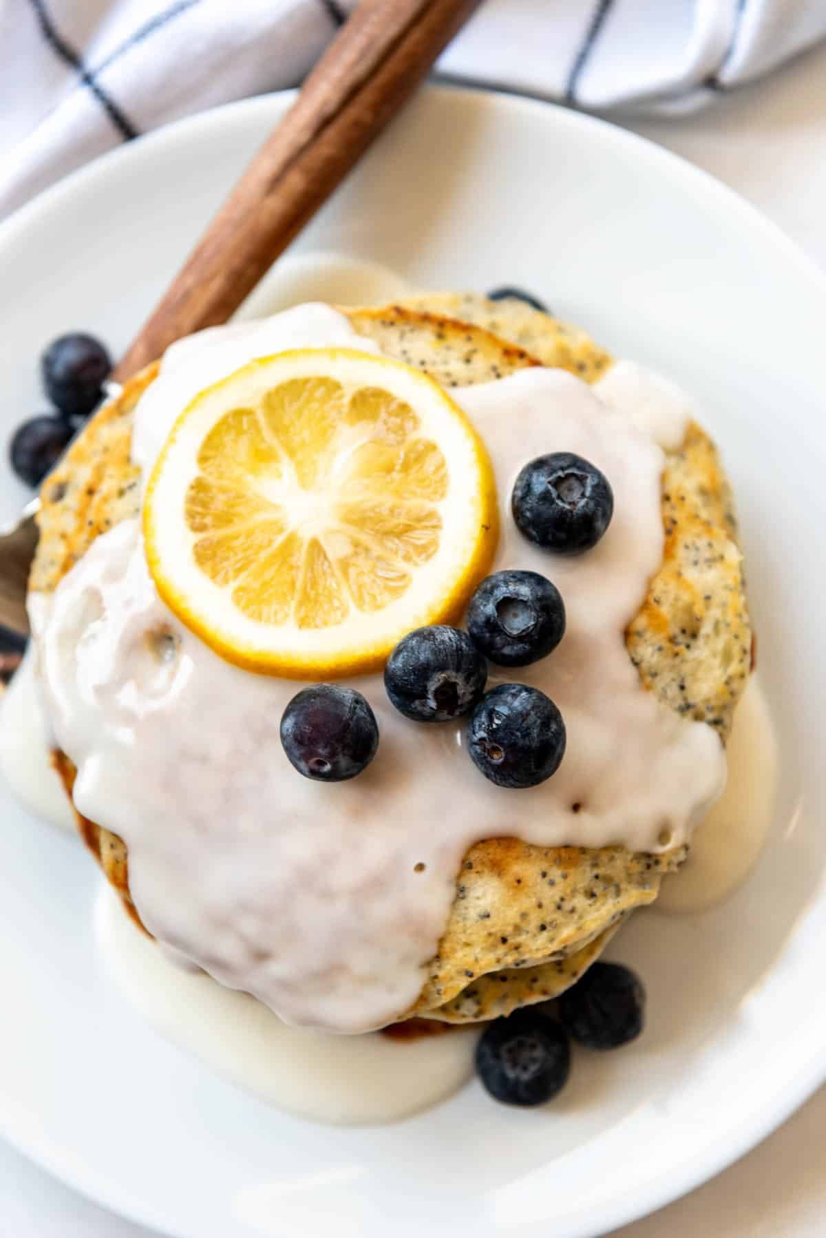 Lemon glaze and blueberries over a stack of pancakes.