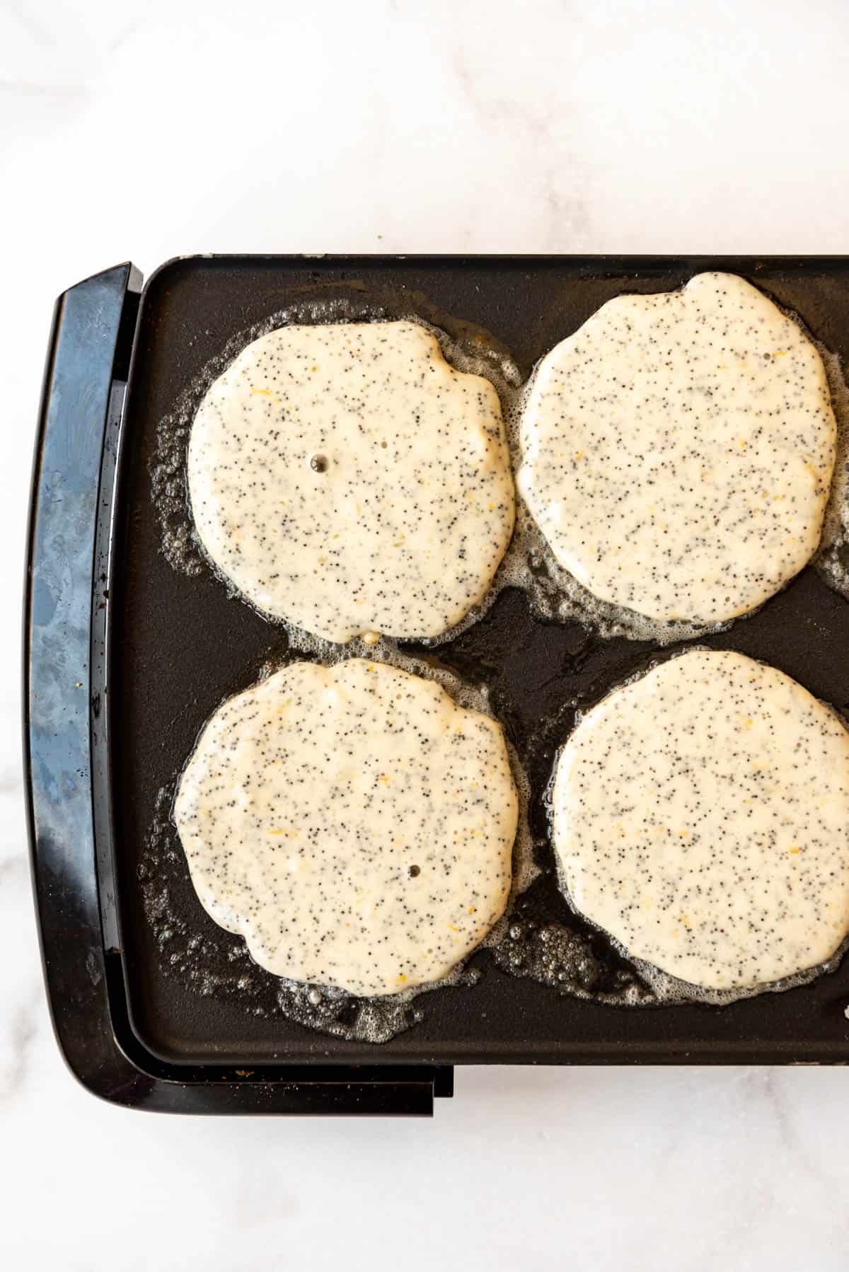 An overhead image of pancakes cooking in butter on a griddle.