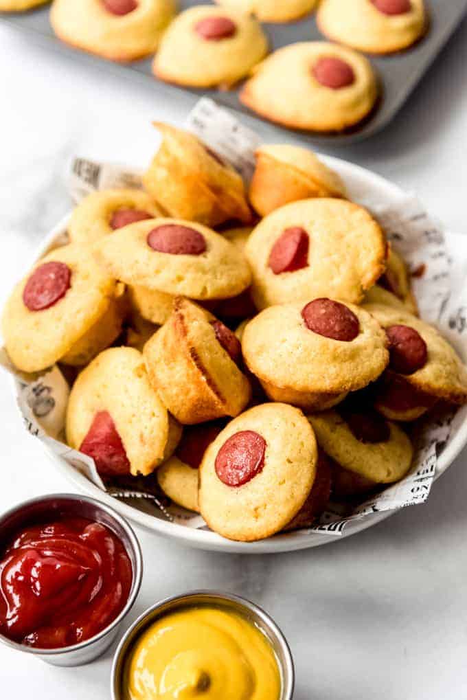 Corn dog muffins next to cups of ketchup and mustard.
