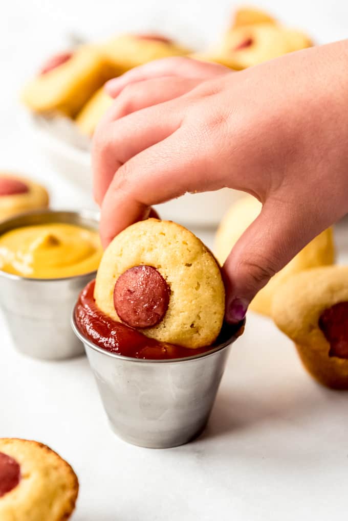 A hand dipping a corn dog mini muffin into ketchup.