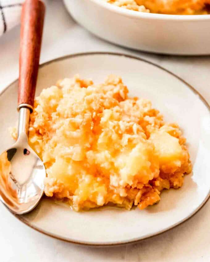 A scoop of pineapple casserole on a plate in front of a casserole dish.