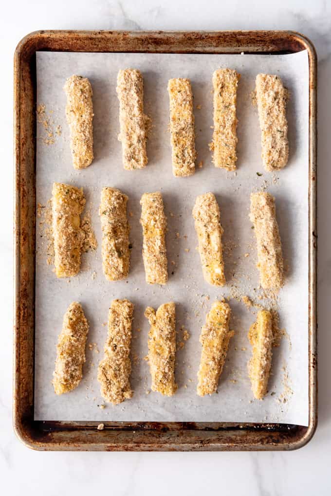 breaded mozzarella sticks on a baking sheet ready to be frozen