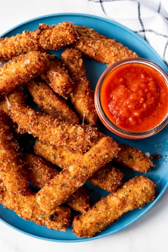 crispy mozzarella sticks on a plate with a cup of marinara sauce for dipping