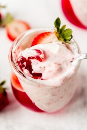 An overhead image of strawberry mousse and jello in a cup with a spoon.