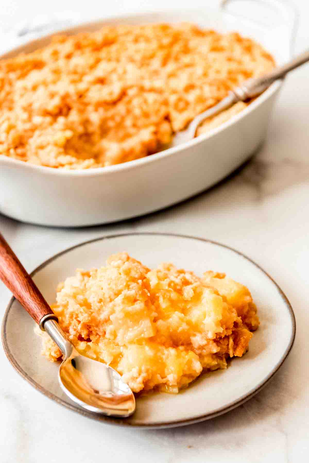 A scoop of pineapple casserole on a plate in front of a casserole dish.