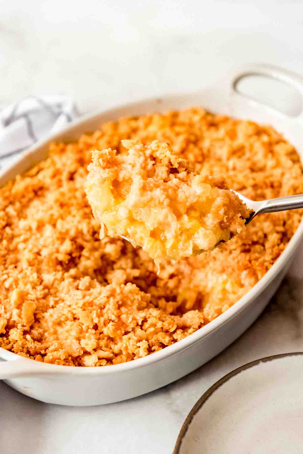 A serving spoon holding a scoop of pineapple casserole.