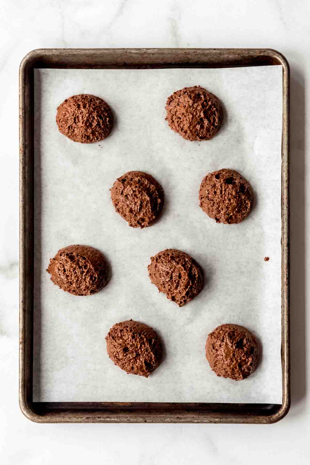 Rounded scoops of batter are placed on a parchment-lined baking sheet. 