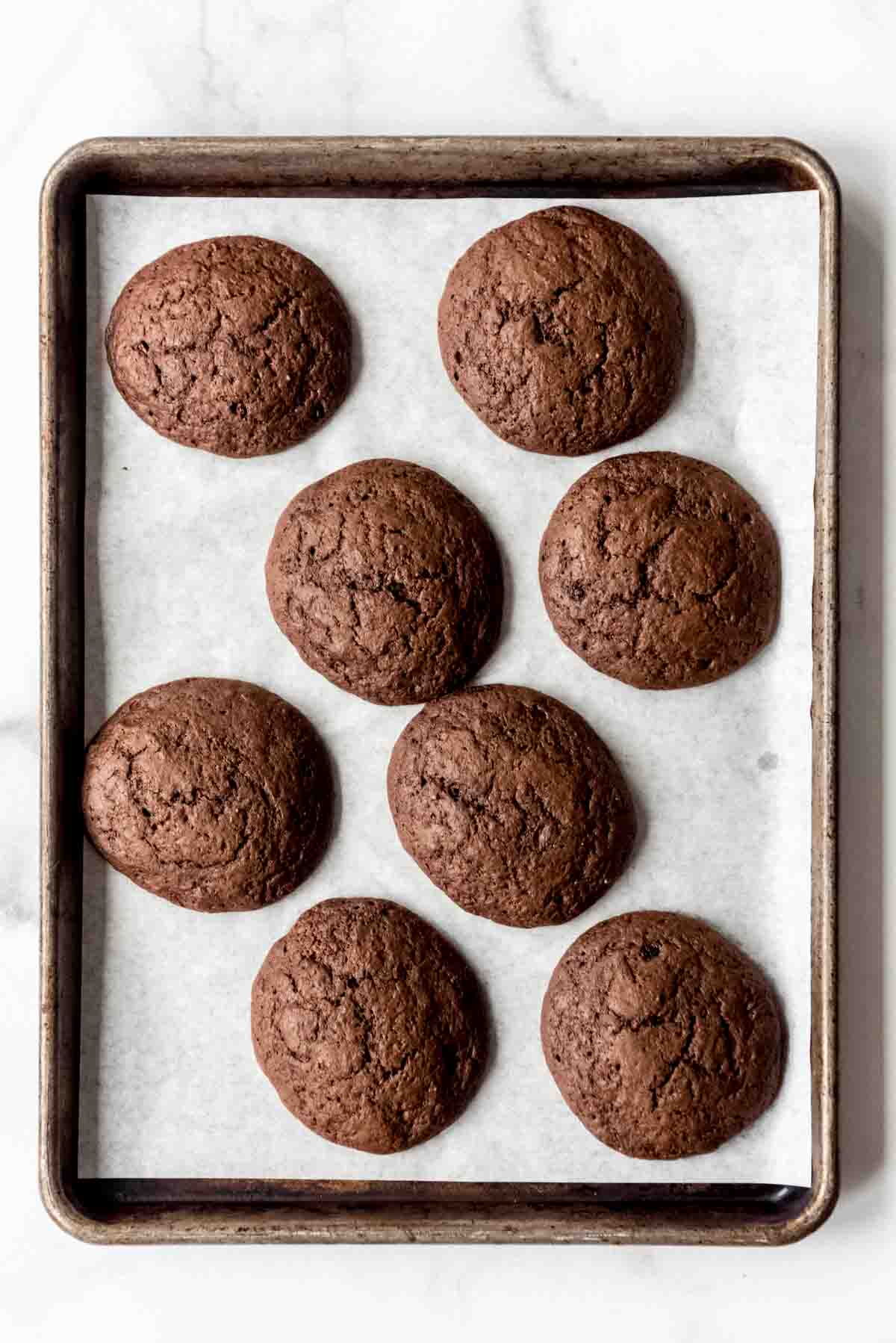 Baked Whoopie Pie treats are resting on a parchment-lined cookie sheet. 