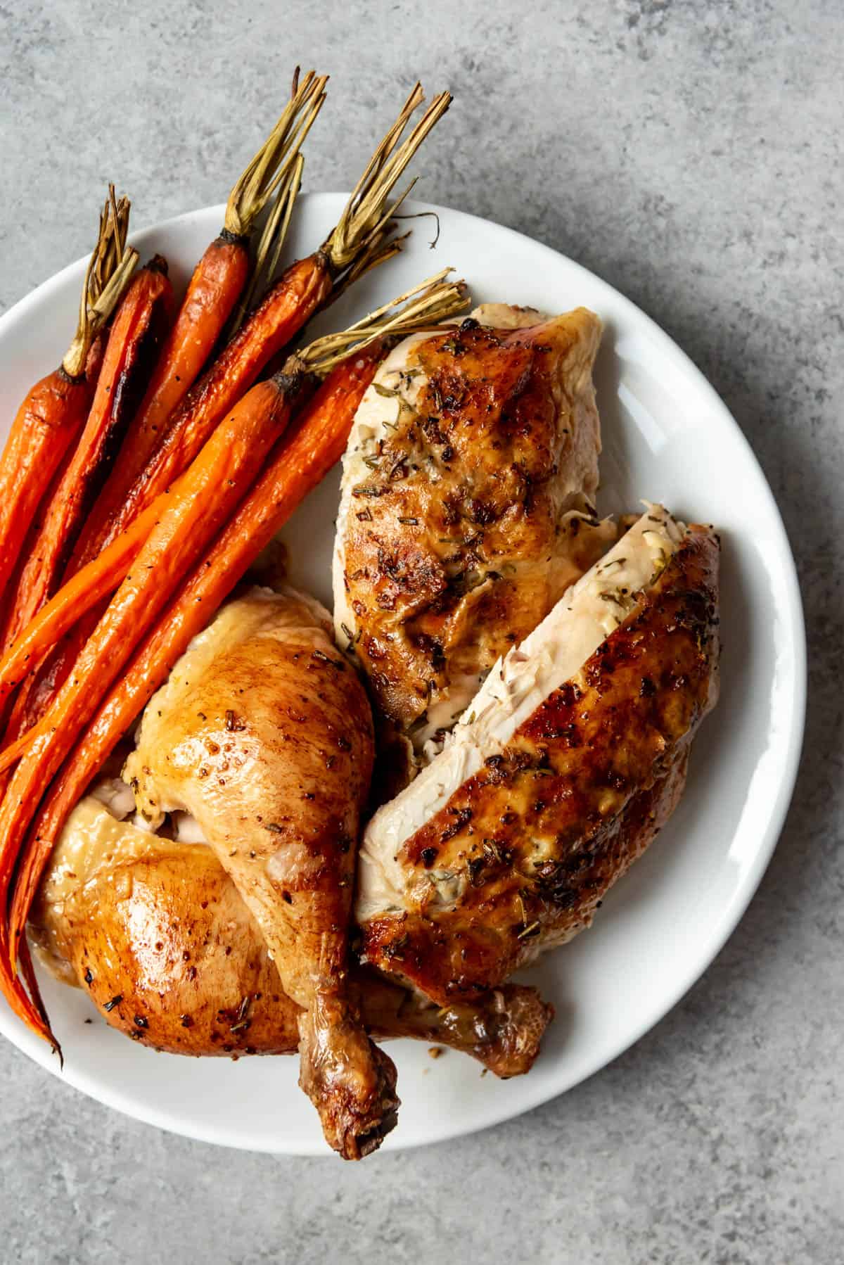 A slow roasted chicken cut up with carrots on white plate.