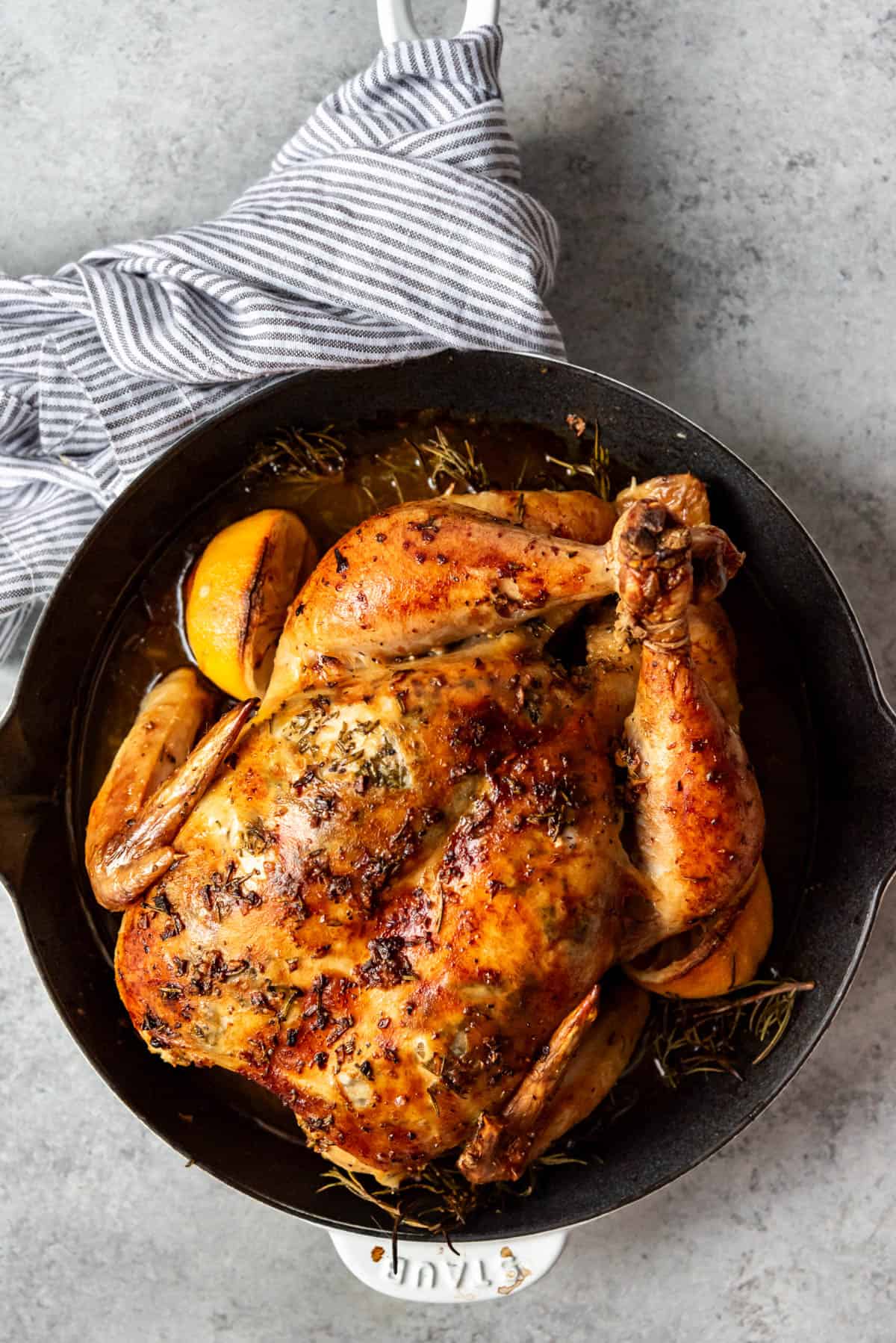 An overhead image of a pan with a roast chicken in it and a striped linen towel wrapped around the pan's handle.