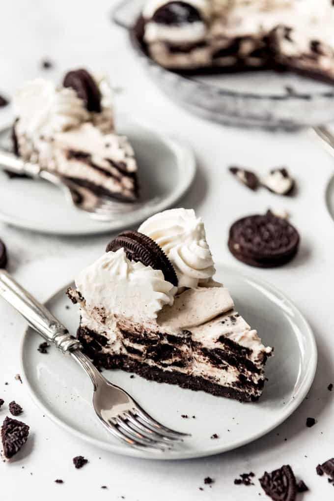 slice of oreo pie on white plate with fork, surrounded by cookies on surface.