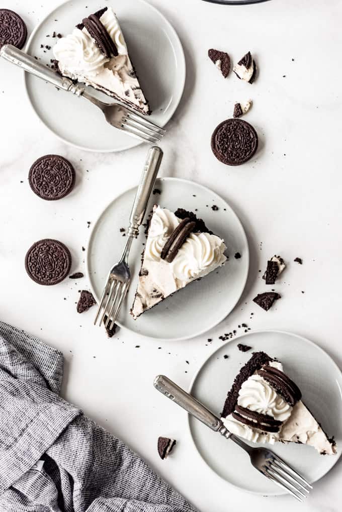 overhead, 3 slices of oreo pies with forks on white plates.