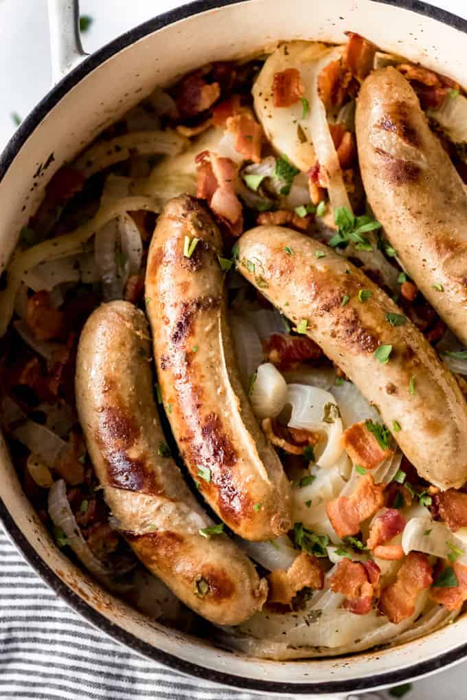 Bangers, potatoes, and onions with bacon in a white pot.