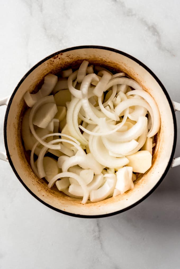 Adding sliced onions to a pot of potatoes and sausages.