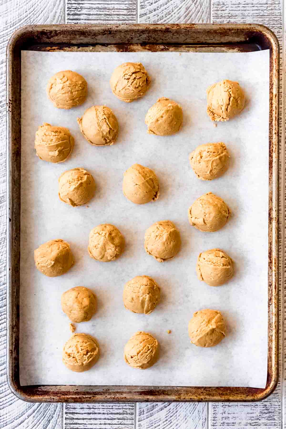 Rounded balls of peanut butter mixture rest on a baking sheet lined with white parchment paper. 