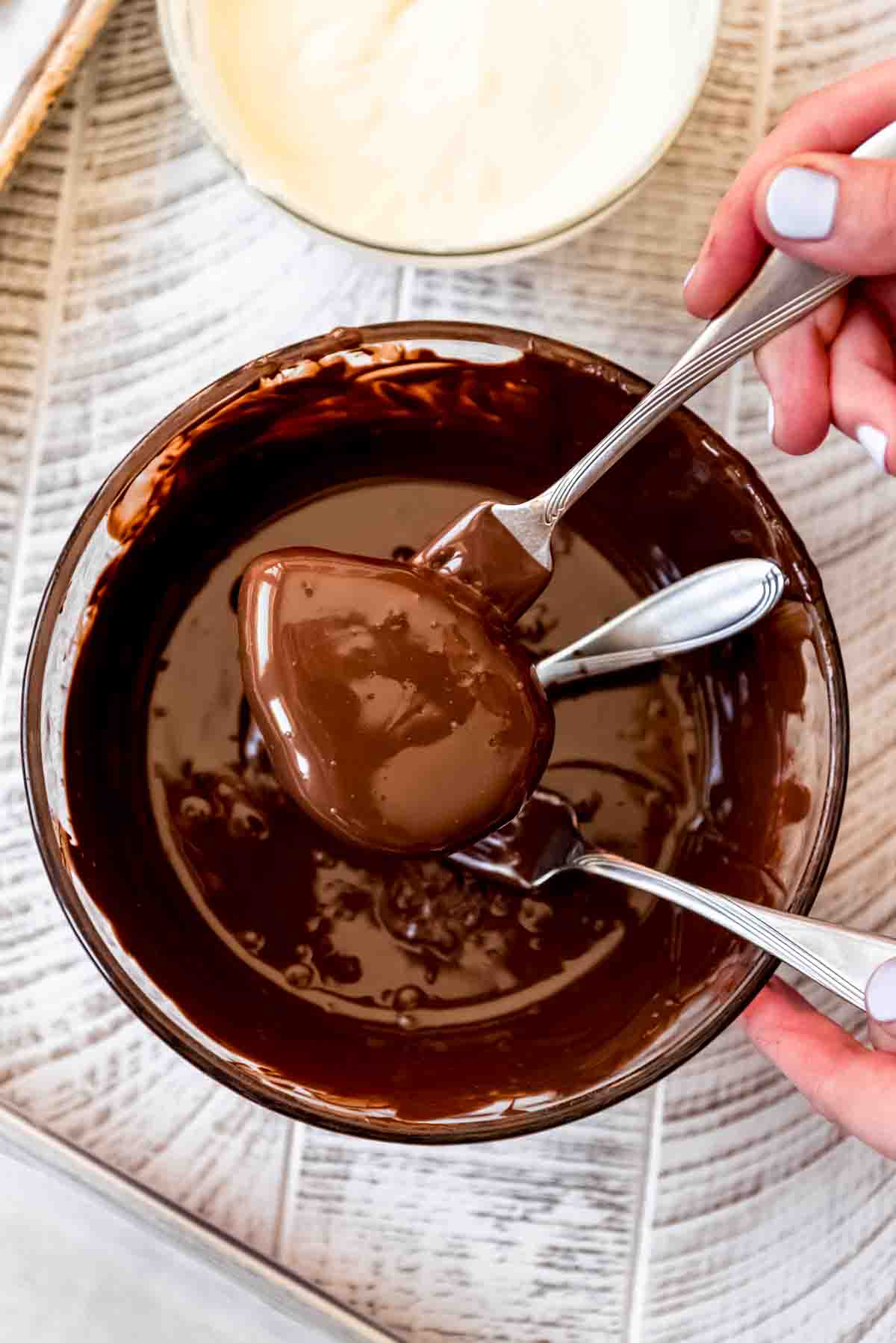 Two forks lifting a peanut butter egg out of melted chocolate.