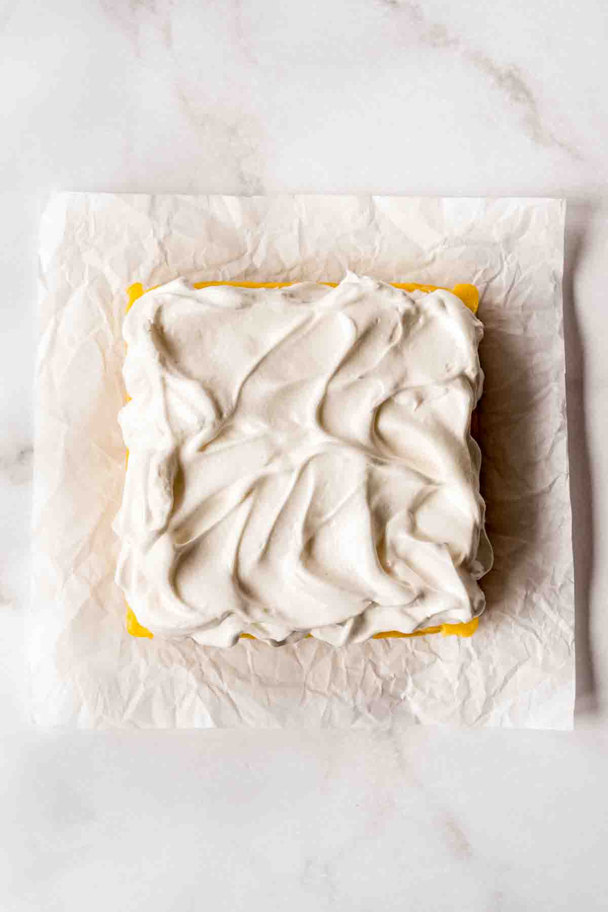 An overhead view of lemon meringue pie bars on a sheet of white parchment, prior to being toasted. 