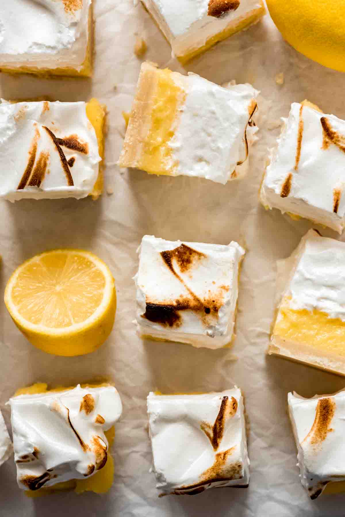 Lemon meringue pie bars cut into squares next to a lemon that has been sliced in half.