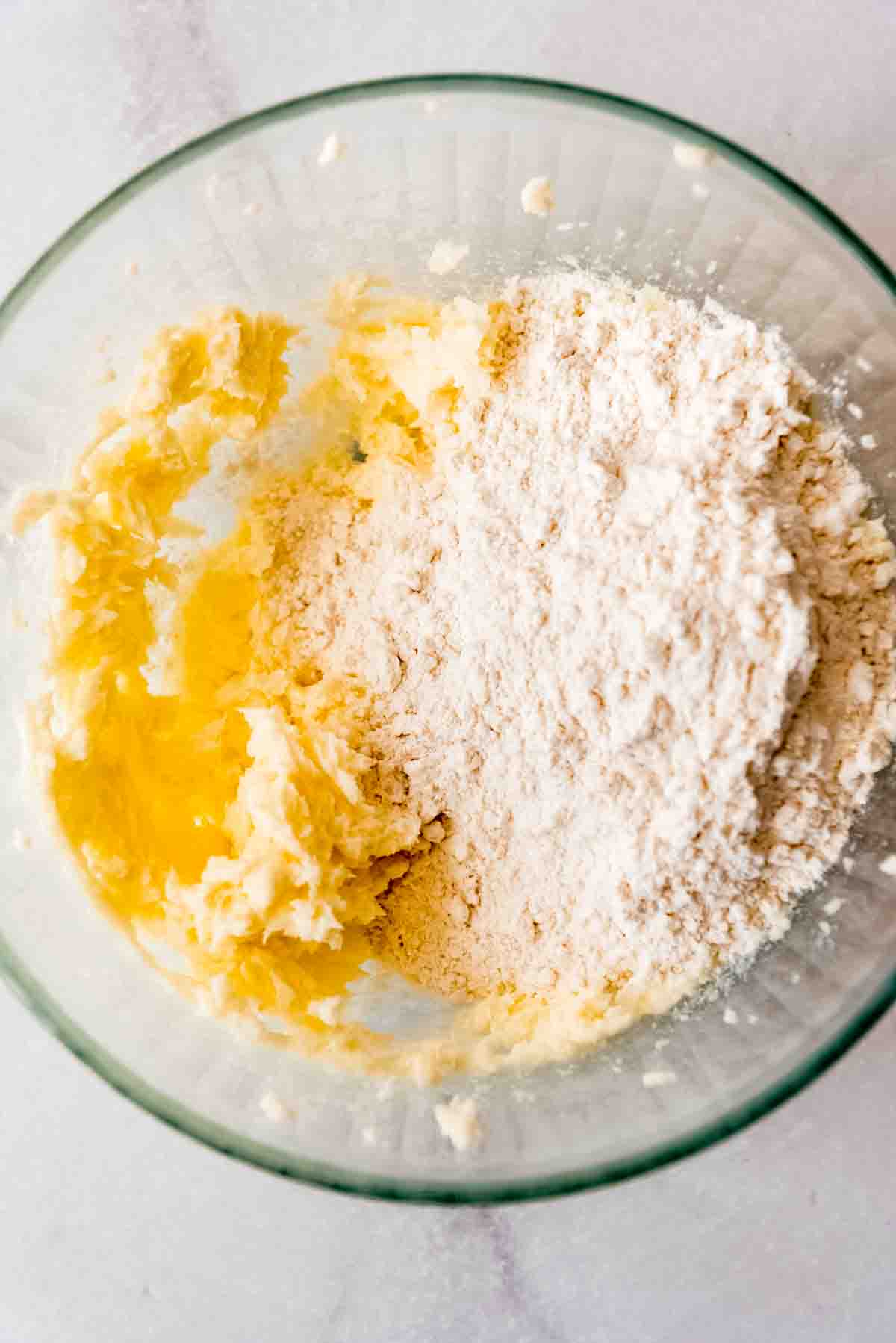 Butter and sugar have been blended in a clear glass bowl, with flour and salt added on top of the mixture. 