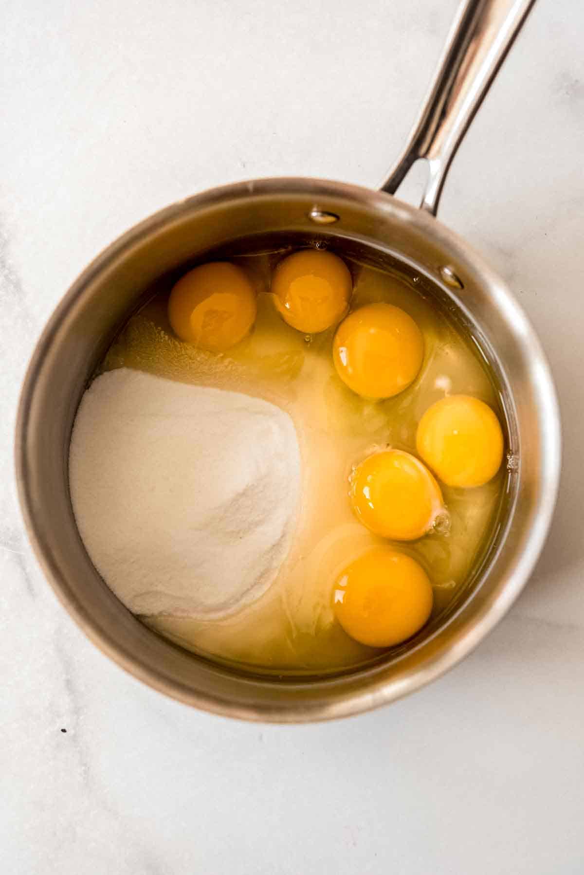 Granulated sugar and eggs are in a metal saucepan, ready to be combined. 