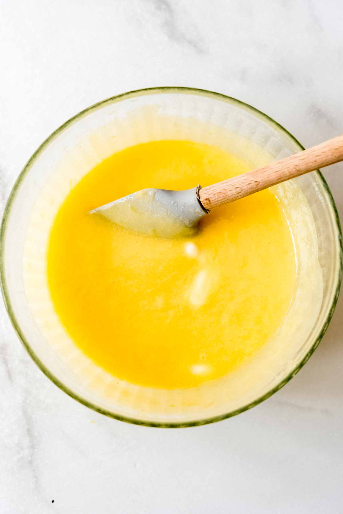 Lemon meringue pie bar filling is stirred with a spatula in a glass bowl. 