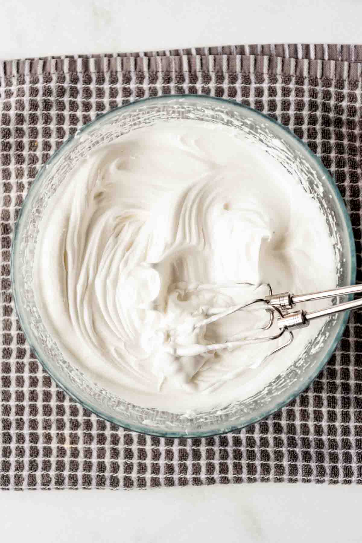 Beaters from a hand mixer are resting on the side of a glass bowl containing meringue topping that has been beaten. 