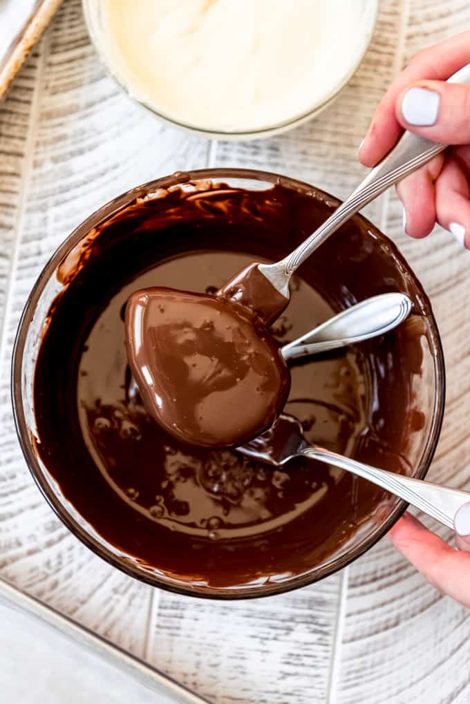 Two forks lifting a peanut butter egg out of melted chocolate.