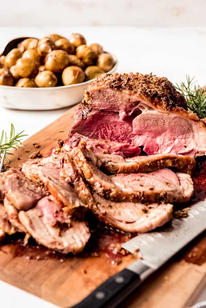 Boneless Leg of Lamb sliced on wooden board with potatoes in background