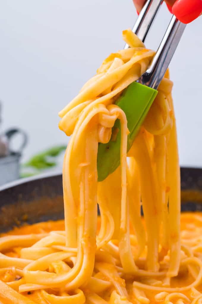 tossing fettuccine pasta in roasted red pepper sauce with tongs