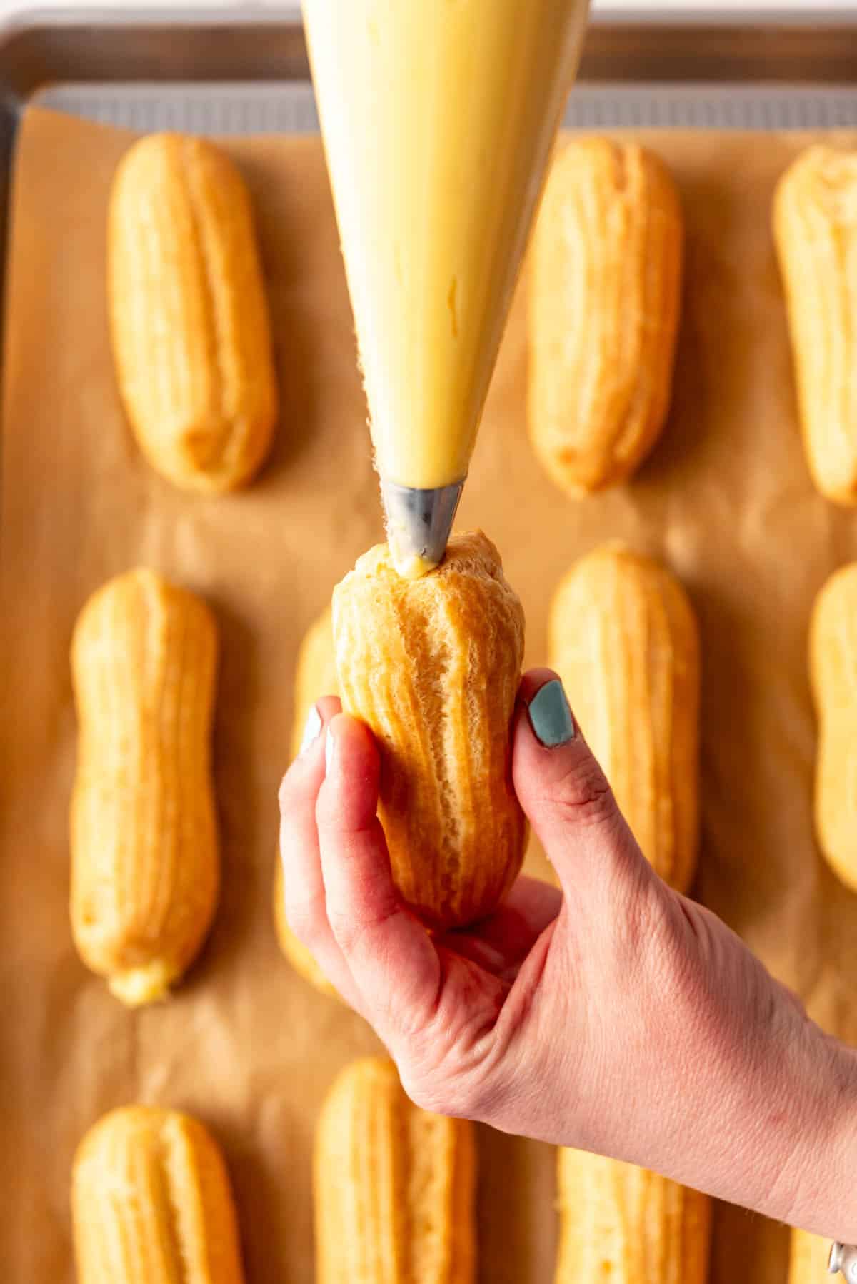 an eclair shell being filled with pastry cream