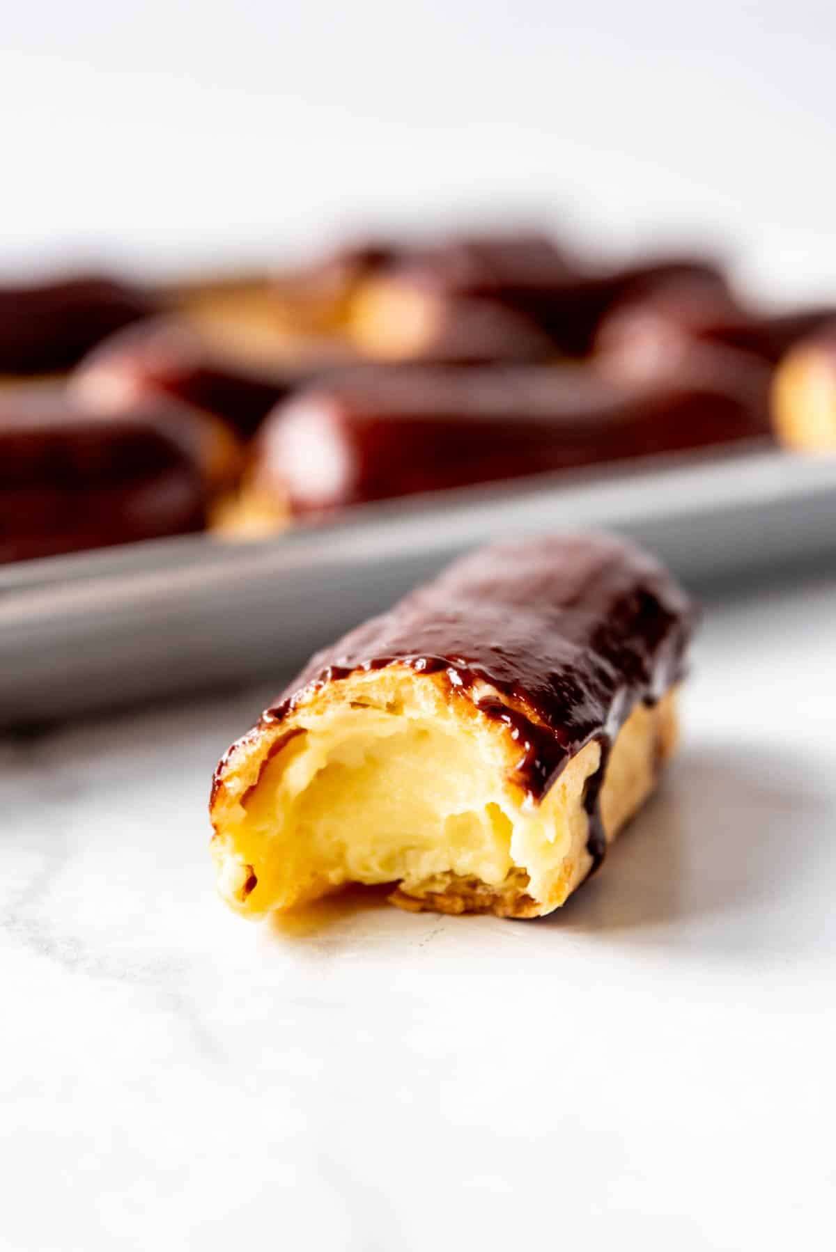 a pastry cream filled chocolate eclair with a bite taken out of it