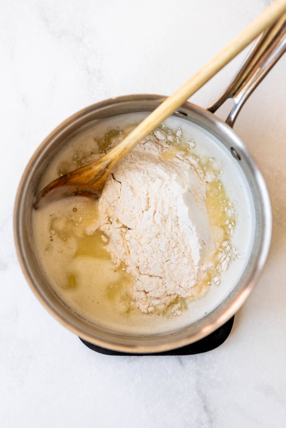 Adding flour to a saucepan of melted butter and water for choux dough.