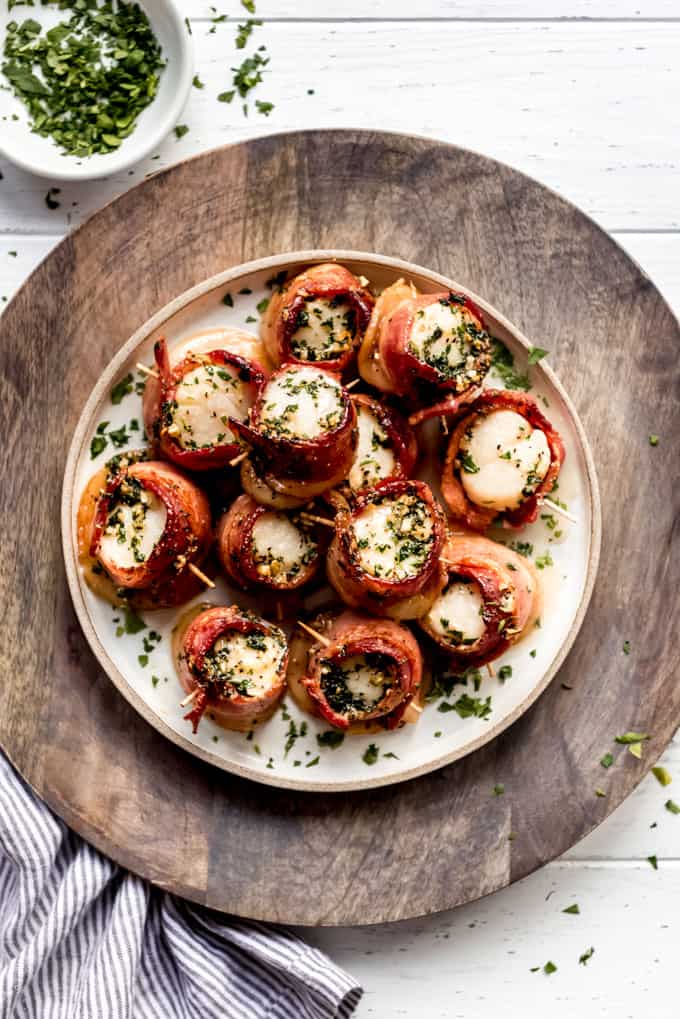 Freshly baked bacon wrapped scallops served on a plate sprinkled with fresh parsley