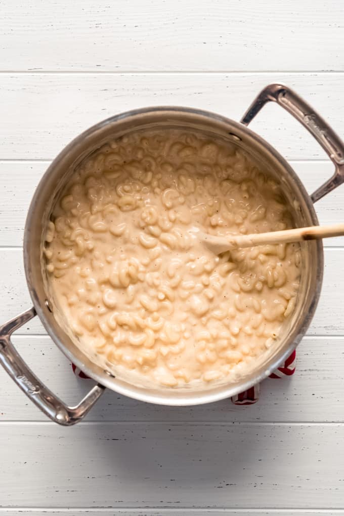 stirring macaroni noodles into a creamy sauce in a large pot
