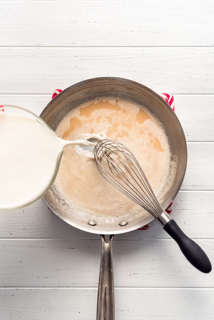 pouring milk into a pan with flour cooked in melted butter