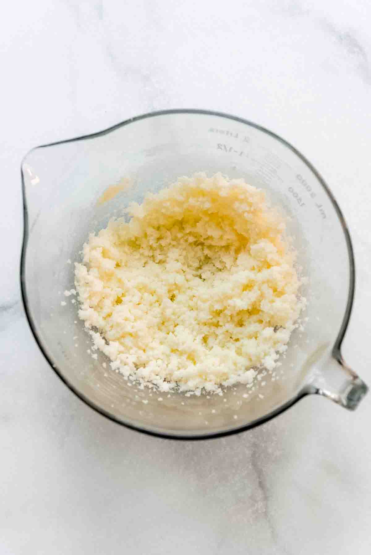 Softened butter and sugar have been creamed together in a glass mixing bowl with a handle and spout. The texture is fluffy. 